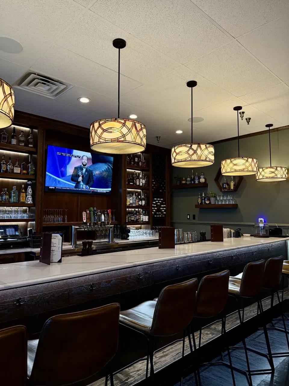 Leather bar stools beneath warm stained-glass pendant lights at Davie Tavern